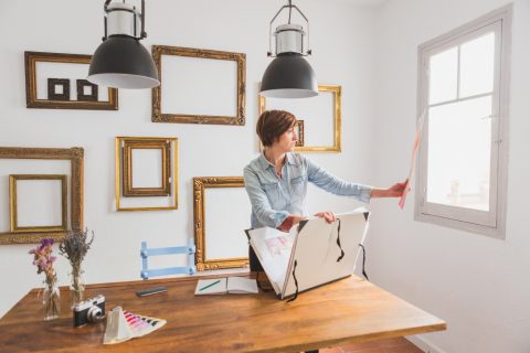 A woman stands in front of a table displaying a large piece of paper, engaged in a discussion or presentation