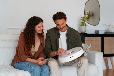 A man and woman sit on a couch, with a white box placed on the coffee table in front of them
