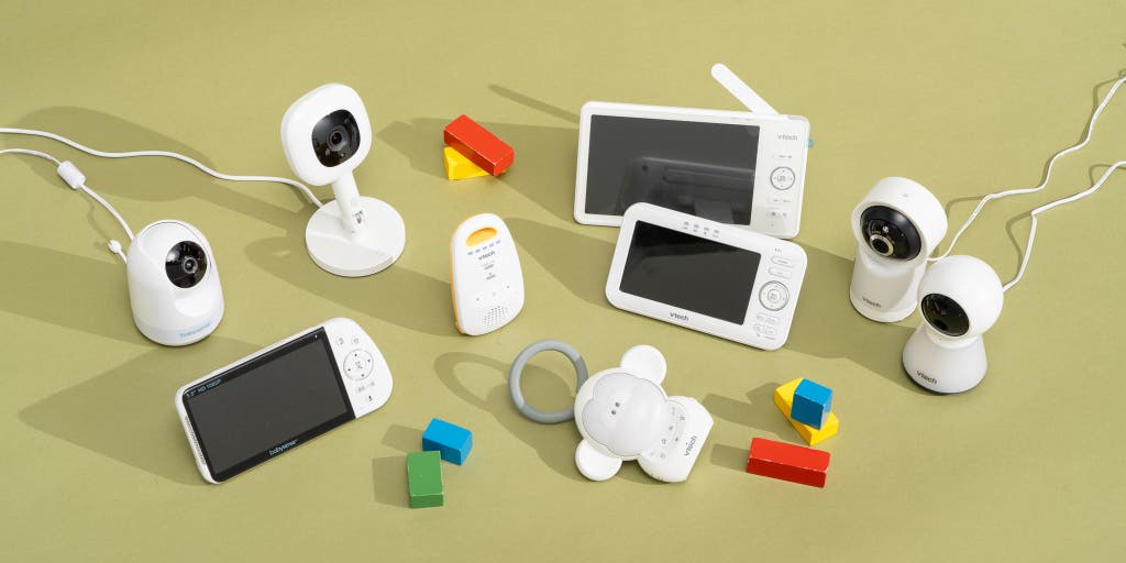 A collection of electronic devices: a baby monitor, a camera, and a smartphone arranged together on a surface