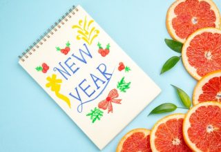New Year design on notebook with grapefruit slices and leaves on light blue background