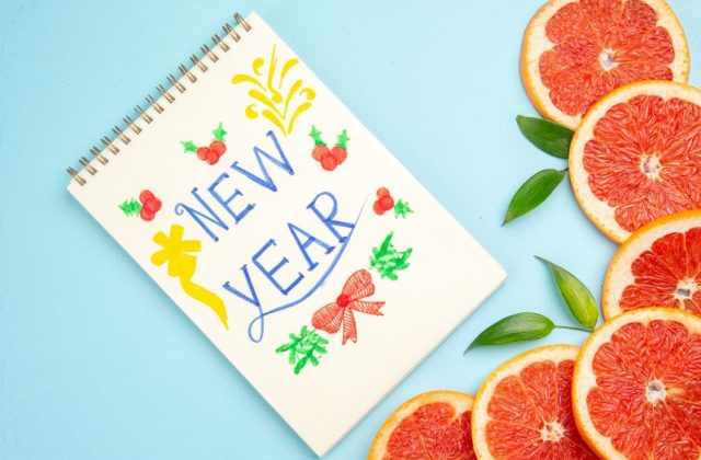 New Year design on notebook with grapefruit slices and leaves on light blue background